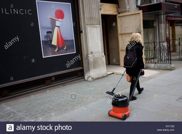 woman-cleaner-pulling-a-vacuum-hover-behind-her-walks-past-a-fashion-DY1T20.jpg